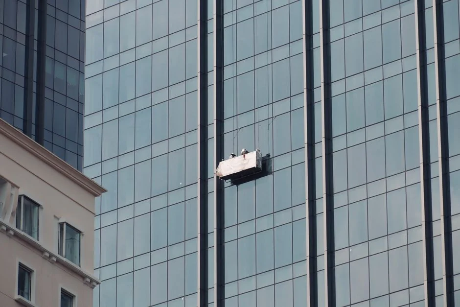 Des laveurs de vitres en hauteur, équipés de matériel de sécurité, nettoient la façade d’un gratte-ciel.